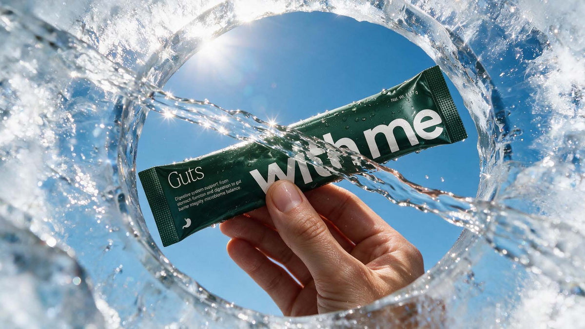 A hand holding the green Guts stick pack through a ring of splashing water against a blue sky