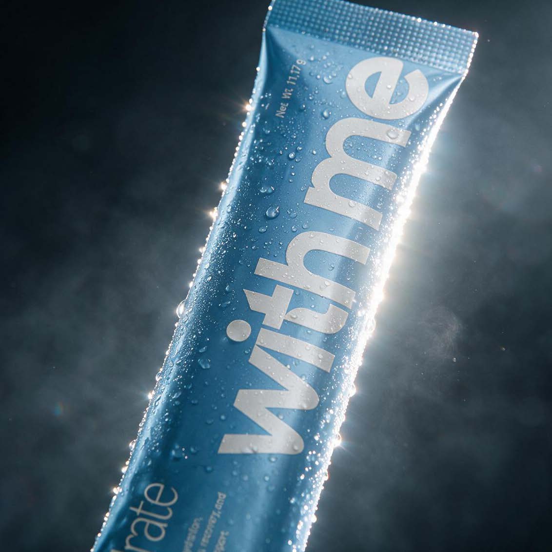 A blue Hydrate stick pack covered in water droplets, backlit against a dark background